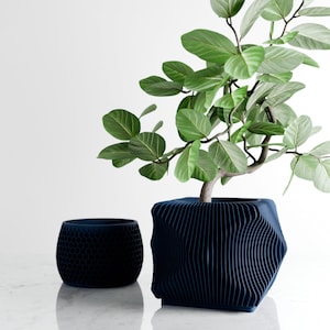 Peut inclure: Deux pots de fleurs bleu foncé, l'un avec un motif en nid d'abeille et l'autre avec un design ondulé, contiennent une plante verte à grandes feuilles. Les pots sont sur une surface blanche, créant une esthétique moderne et minimaliste.