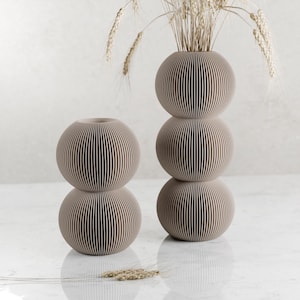 May include: Two beige ceramic vases with a ribbed design. The taller vase has three stacked spheres and the shorter vase has two stacked spheres.