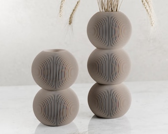 May include: Two beige ceramic vases with a ribbed design. The taller vase has three stacked spheres and the shorter vase has two stacked spheres.