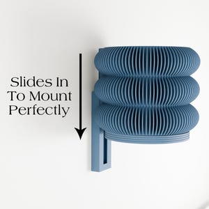 May include: A blue wall-mounted light fixture with a unique, layered design. The fixture has three stacked, ribbed sections that create a textured appearance. The text "Slides In To Mount Perfectly" is displayed on the left side of the image.
