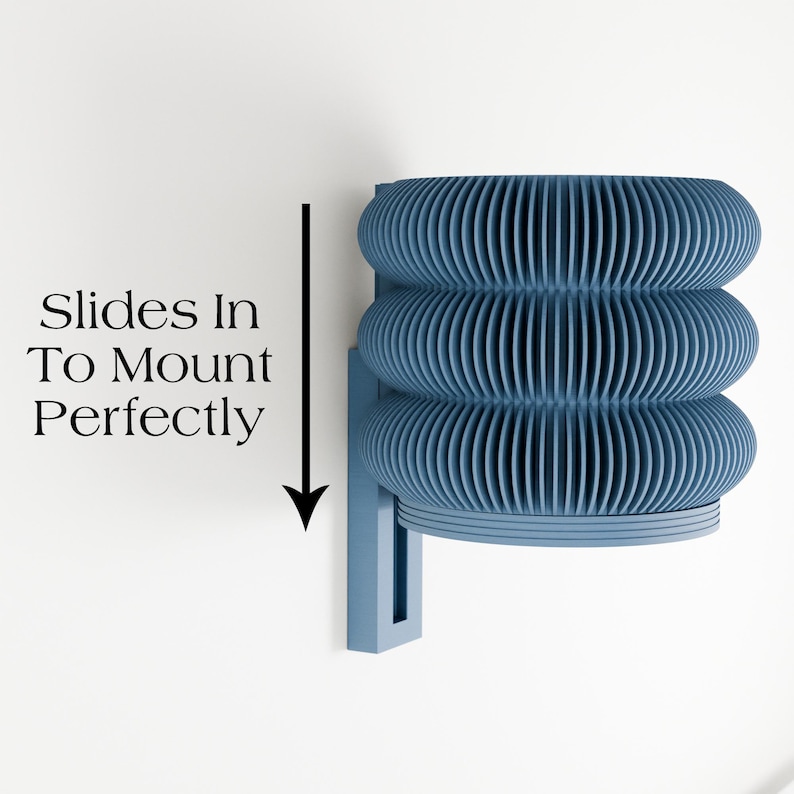 May include: A blue wall-mounted light fixture with a unique, layered design. The fixture has three stacked, ribbed sections that create a textured appearance. The text "Slides In To Mount Perfectly" is displayed on the left side of the image.