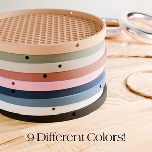 May include: A stack of nine round coasters in various colors, including beige, green, white, pink, blue, and black. Each coaster has a textured surface and a small hole. The text "9 Different Colors!" is displayed below.