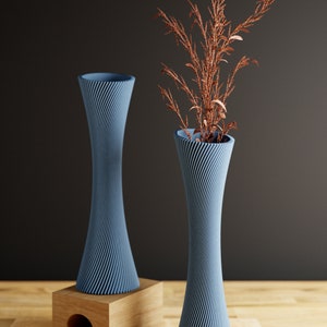 May include: Two blue ceramic vases with a swirling pattern. The vase on the right is taller and has a sprig of dried brown foliage in it. The vases are on a wooden surface.