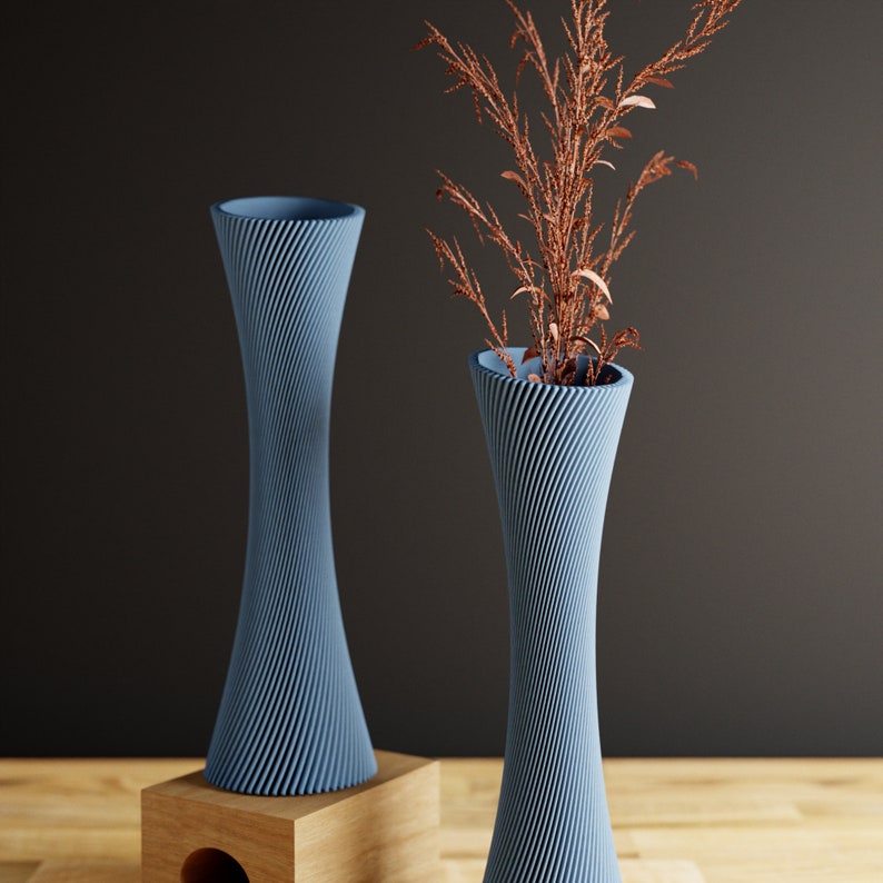 May include: Two blue ceramic vases with a swirling pattern. The vase on the right is taller and has a sprig of dried brown foliage in it. The vases are on a wooden surface.