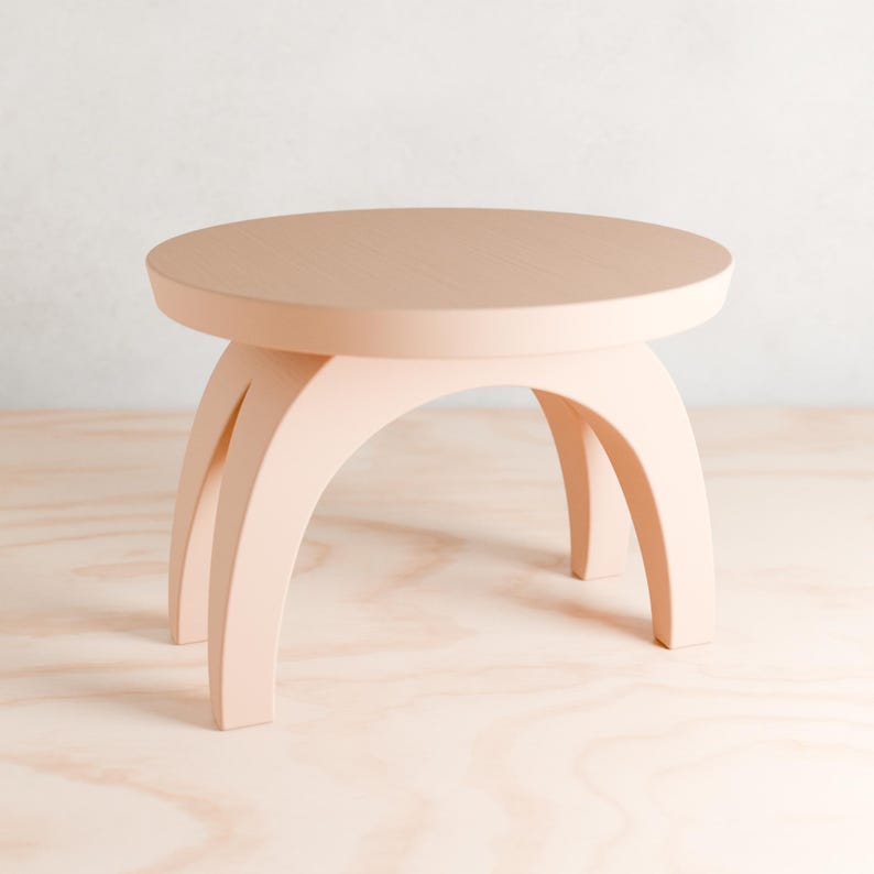 May include: A light pink round table with three arched legs. The table is made of wood and has a smooth surface.