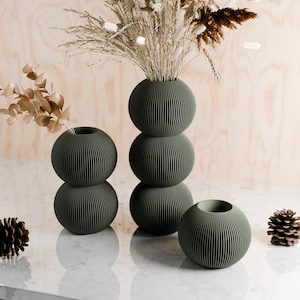 May include: Three green ceramic vases with a ribbed texture. The tallest vase is stacked with three round sections. The other two vases are each two round sections stacked on top of each other.