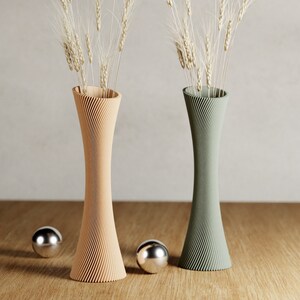May include: Two decorative vases with a swirling pattern, one in a light brown color and the other in a green color. Both vases are filled with dried wheat stalks.