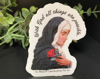 Puede incluir: Una pegatina blanca con una imagen de una mujer con hábito negro sosteniendo una rosa roja. El texto "With God all things are possible." está escrito en un círculo alrededor de la mujer. El texto "St. Rita of Cascia, pray for us." está escrito debajo de la mujer.
