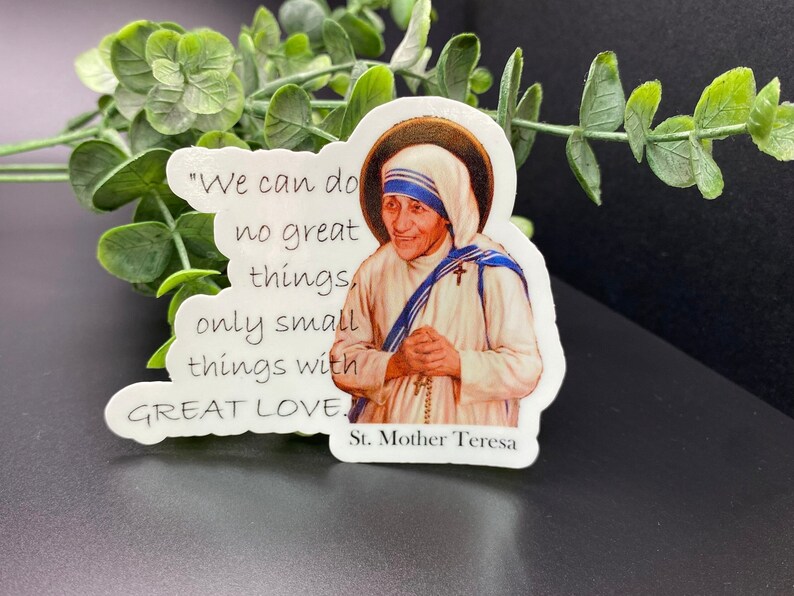 Puede incluir: Una pegatina blanca con una cita de la Madre Teresa: "No podemos hacer grandes cosas, solo peque&ntilde;as cosas con GRAN AMOR." La pegatina presenta un retrato de la Madre Teresa con un h&aacute;bito blanco y una faja azul.