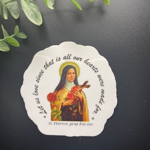 Puede incluir: Una pegatina blanca con una imagen colorida de Santa Teresa de Lisieux sosteniendo un ramo de rosas. El texto en la pegatina dice "Amemos porque para eso fueron hechos nuestros corazones." y "Santa Teresa, reza por mí."