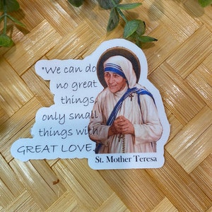 Puede incluir: Una pegatina blanca con una cita de la Madre Teresa: "No podemos hacer grandes cosas, solo peque&ntilde;as cosas con GRAN AMOR." La pegatina presenta una foto de la Madre Teresa con una cubierta de cabeza blanca y un sari azul y blanco. El texto "Santa Madre Teresa" est&aacute; impreso debajo de la cita.