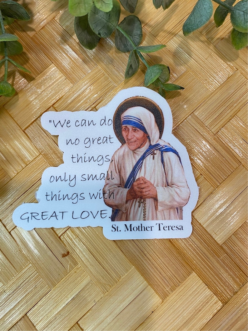 Puede incluir: Una pegatina blanca con una cita de la Madre Teresa: "No podemos hacer grandes cosas, solo peque&ntilde;as cosas con GRAN AMOR." La pegatina presenta una foto de la Madre Teresa con una cubierta de cabeza blanca y un sari azul y blanco. El texto "Santa Madre Teresa" est&aacute; impreso debajo de la cita.