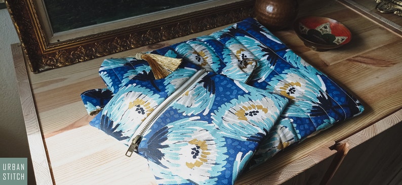 May include: A set of three blue and white floral patterned zippered pouches with gold tassels. The pouches are made of fabric and have a quilted texture.