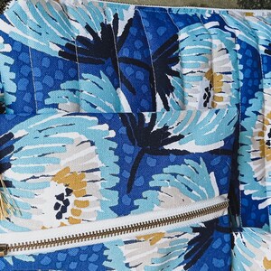 May include: A blue and white floral patterned zippered pouch with a gold tassel. The pouch is quilted and has a white zipper.