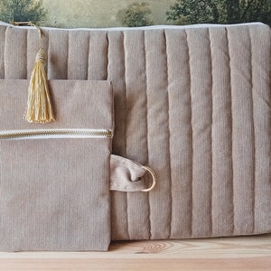 May include: Two beige corduroy zippered pouches with gold zippers and tassels. The larger pouch has a quilted design. The pouches are on a wooden surface.