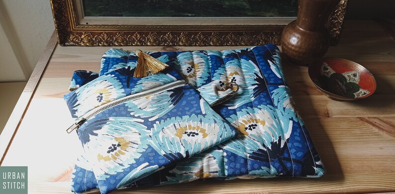 May include: Three blue and white floral patterned zippered pouches with gold tassels. The pouches are arranged on a wooden surface.