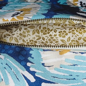 May include: A blue and white floral zippered pouch with a gold tassel. The pouch is open, revealing a gold floral lining.