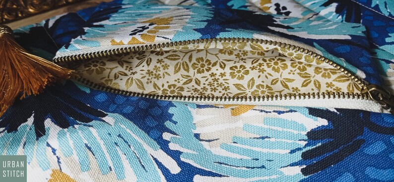 May include: A blue and white floral zippered pouch with a gold tassel. The pouch is open, revealing a gold floral lining.