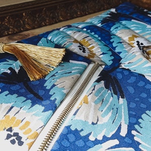 May include: A blue and white zippered pouch with a gold tassel. The pouch has a floral pattern with blue, white, and yellow flowers.
