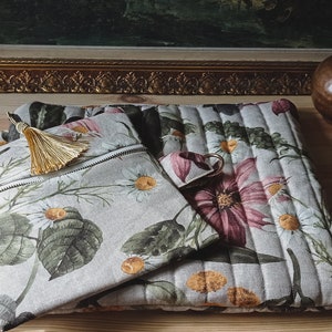 May include: Two floral patterned zippered pouches, one larger than the other, with a gold tassel on the smaller pouch. The pouches are made of a light beige linen fabric with a quilted design.