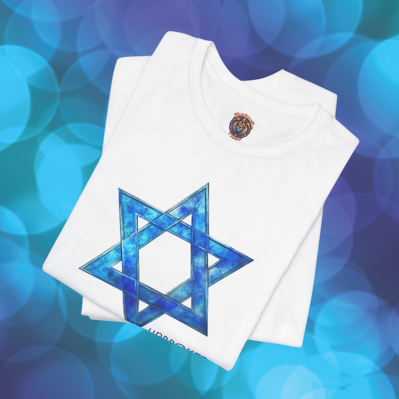 Pu&ograve; includere: T-shirt bianco con un design blu della Stella di David. La stella a sei punte ha un effetto acquerello. La maglietta &egrave; piegata, con un piccolo emblema vicino al colletto. Lo sfondo &egrave; un bokeh blu e bianco.