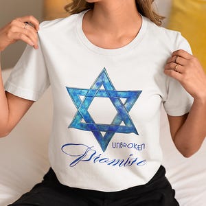 Pu&ograve; includere: T-shirt bianca con un disegno blu della Stella di David con effetto acquerello. Il testo "UNBROKEN Promise" &egrave; scritto in blu sotto la stella. La maglietta ha maniche corte.