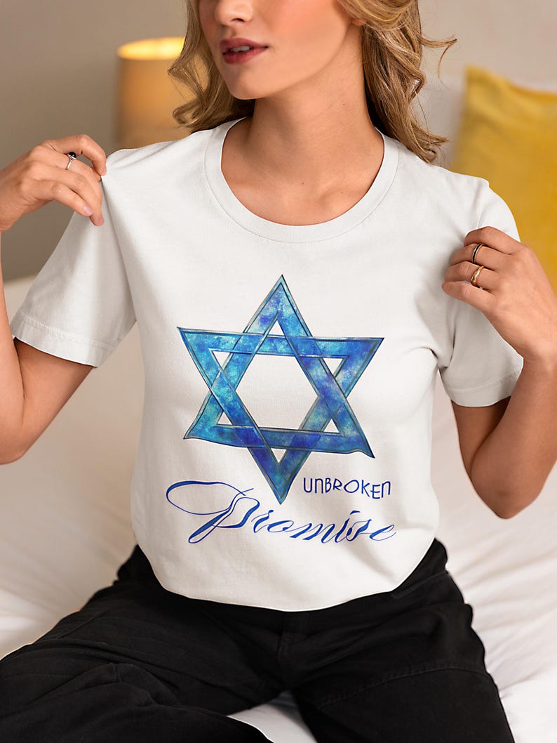 Pu&ograve; includere: T-shirt bianca con un disegno blu della Stella di David con effetto acquerello. Il testo "UNBROKEN Promise" &egrave; scritto in blu sotto la stella. La maglietta ha maniche corte.