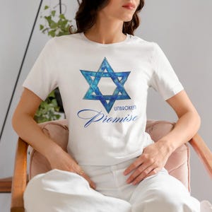 Pu&ograve; includere: T-shirt bianca con un disegno blu della Stella di David e le parole "UNBROKEN Promise". La Stella di David ha un effetto acquerello. La maglietta &egrave; a maniche corte e realizzata in un materiale morbido.