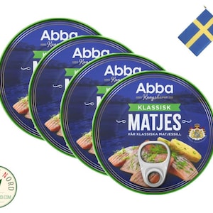May include: Three cans of Abba Kungshamn Klassisk Matjes herring in brine. The cans are blue with green lids and feature a picture of herring fillets with dill and a Swedish flag.