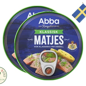 May include: Two cans of Abba Matjes herring in brine, with a green lid and a blue label. The label says "Abba Kungshamn Klassisk Matjes Var Klassiska Matjessill".