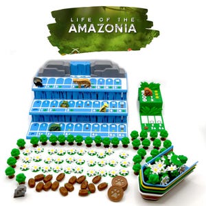 Może przedstawiać: Gra planszowa zatytułowana "Life of the Amazonia" z niebieską, warstwową planszą do gry, figurkami zwierząt, zielonymi drzewami, białymi kwiatami i brązowymi żetonami. Gra zawiera zielony element punktacji i wielokolorowy pojemnik.