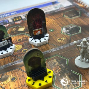May include: A board game with various game pieces, including a yellow hexagonal piece with numbers, a white hexagonal piece with a black number, and a gray figurine. The game board has a wooden texture with hexagonal spaces.