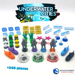 Op de afbeelding: Een verzameling spelonderdelen van het bordspel "Underwater Cities". De afbeelding toont miniatuur onderzeeërs, duikersfiguren, koepelvormige structuren en diverse tokens. Het kleurenpalet bevat blauwe, oranje, paarse, groene en grijze elementen. De spelset bevat +340 stukken.