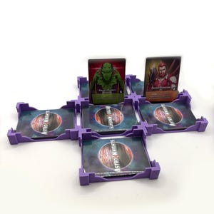 Puede incluir: Un juego de mesa con tarjeteros morados y cartas de personajes. Las cartas de personajes presentan ilustraciones de un alienígena verde y un guerrero pelirrojo. Los tarjeteros tienen el texto "ASTRO KNIGHTS".