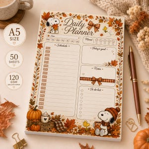 May include: A rectangular A5 daily planner notepad featuring a Snoopy and Woodstock autumn theme with orange and brown fall leaves. The page includes sections for a schedule from 7AM to 11PM, a mood tracker, today's goal, notes, and a to-do list.