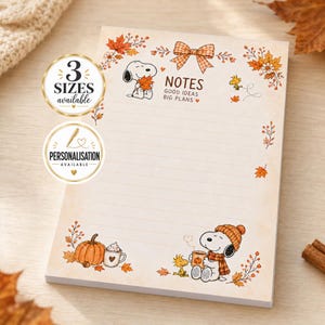 May include: A rectangular notepad with a cream background and autumn-themed illustrations of Snoopy and Woodstock. The top features a plaid bow and the text "NOTES GOOD IDEAS BIG PLANS". The border includes orange leaves, pumpkins, and mugs.