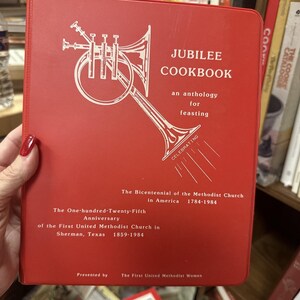 Puede incluir: Cubierta de libro de cocina roja con una ilustración de trompeta blanca y el título "JUBILEE COOKBOOK" en texto blanco. El subtítulo dice "una antología para darse un festín". El texto debajo del título dice "Celebrando el bicentenario de la Iglesia Metodista en América 1784-1984. El 125 aniversario de la Primera Iglesia Metodista Unida de Sherman, Texas 1859-1984. Presentado por las mujeres de la Primera Iglesia Metodista Unida."