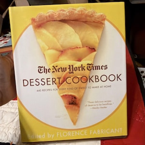 May include: A yellow cookbook titled "The New York Times Dessert Cookbook" with a large illustration of a pie slice. The book cover includes the text "440 Recipes for Every Kind of Sweet to Make at Home" and is edited by Florence Fabricant.