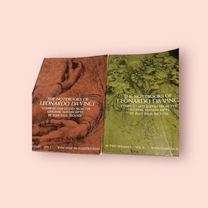 Puede incluir: Dos libros de tapa dura marrón y verde titulados "The Notebooks of Leonardo da Vinci" con el texto "Compiled and edited from the original manuscripts by Jean Paul Richter" en la portada. El libro de la izquierda es el volumen 1 y el libro de la derecha es el volumen 2. Ambos libros tienen más de 700 ilustraciones.