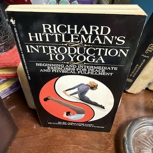 May include: A hardcover book titled "RICHARD HITTLEMAN'S INTRODUCTION TO YOGA" with a black cover and white text. The cover features a yin-yang symbol with yoga poses. The book is a guide to yoga exercises for peace and physical fulfillment.