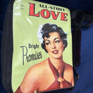 May include: A black messenger bag with a retro magazine cover design. The cover features a woman in a red dress with the words "ALL-STORY LOVE" and "Bright Promises". The bag has a black shoulder strap and a padded shoulder rest.