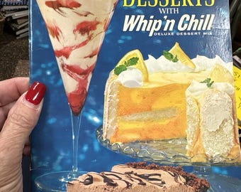 Op de afbeelding: Een vintage doos Whip 'n Chill Deluxe Dessert Mix. De doos heeft een kleurrijke illustratie van drie desserts: een chocoladetaart, een citroencake en een aardbeienparfait. De tekst op de doos luidt "Magical Desserts with Whip 'n Chill Deluxe Dessert Mix".
