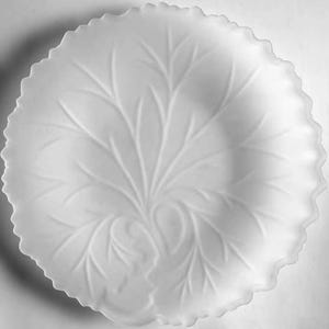 May include: A round, white, translucent glass plate featuring a molded, raised relief pattern of a large, central leaf with intricate veins spreading outward toward the scalloped, ruffled edges of the dish, creating a textured surface.