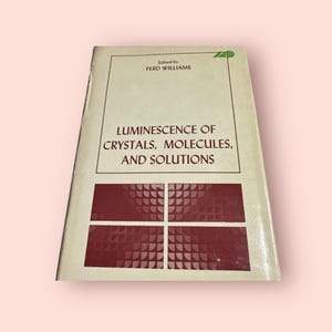May include: A book titled "Luminescence of Crystals, Molecules, and Solutions" edited by Ferd Williams. The cover is beige with a red design of four squares with a pattern of small circles.