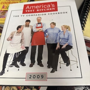 May include: A cookbook titled "America's Test Kitchen: The TV Companion Cookbook" with a group of people in aprons and chef coats. The year "2009" is printed at the bottom of the cover.