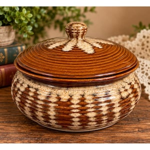 May include: A round, lidded ceramic jar featuring a glossy brown glaze with horizontal ribbed textures. The exterior and lid are decorated with a repeating cream-colored, sponge-like pattern that creates a vertical, textured visual effect.