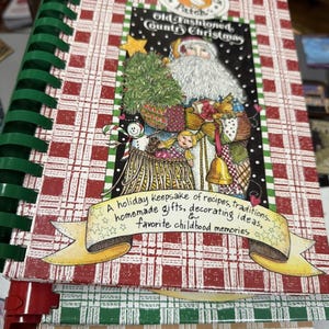 Puede incluir: Un libro de cocina encuadernado en espiral titulado "Gooseberry Patch's Old Fashioned Country Christmas". La portada presenta una ilustración de Papá Noel con un árbol de Navidad y una pancarta que dice "A holiday keepsake of recipes, traditions, homemade gifts, decorating ideas, & favorite childhood memories."