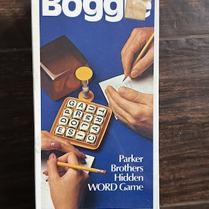 Puede incluir: Caja de juego de palabras Boggle vintage con fondo azul. La caja presenta el logotipo del juego, un tablero y ilustraciones de manos jugando. También se ve el texto "Parker Brothers Hidden WORD Game".