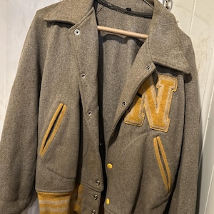 May include: A vintage grey wool varsity jacket with a yellow felt letter 'N' on the back. The jacket has yellow and white striped ribbing at the cuffs and hem.
