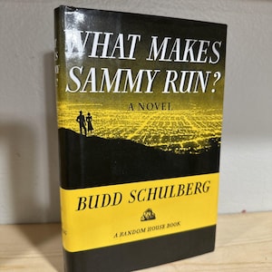 May include: A black and yellow paperback book titled "What Makes Sammy Run? A Novel" by Budd Schulberg. The book cover features a silhouette of a couple standing on a hill overlooking a city at night.
